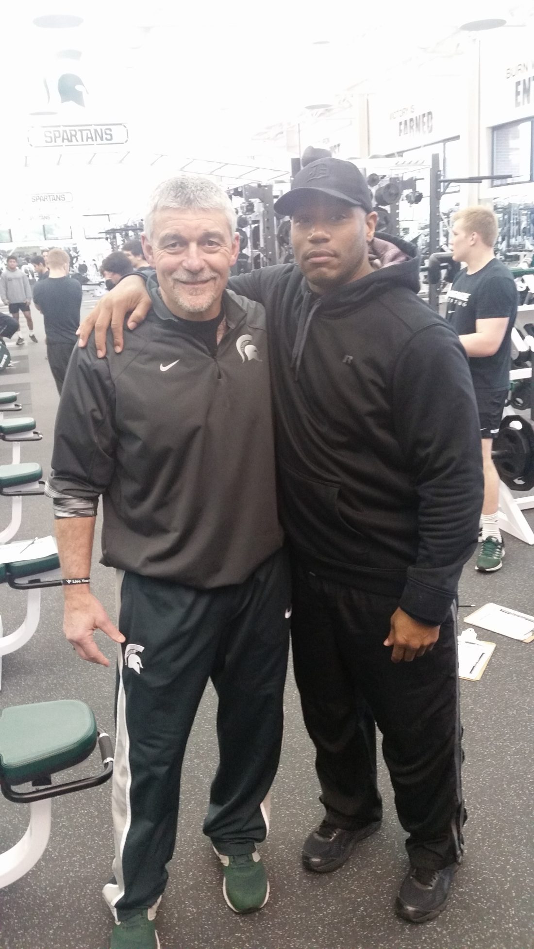 Coach Mannie with his arm around a former player in the weight room